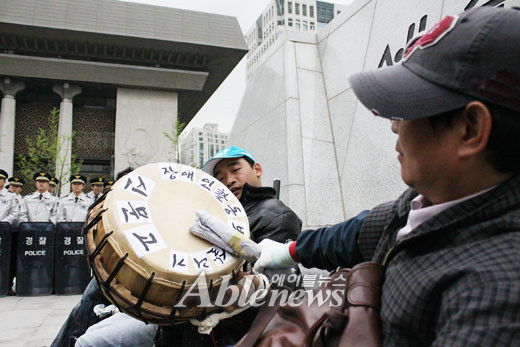 장애인들이 지난 5월 4일 광화문광장 세종대왕 동상앞에서 '장애인활동보조살리기 신문고를 울려라'를 진행하고 있다. '불법 집회'라는 이유로 경찰로부터 북채를 빼앗긴 장애인이 신문지를 말아 신문고를 두들리고 있는 모습. ⓒ에이블뉴스   