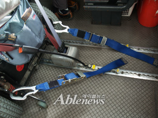 홍콩의 장애인 버스 내부 바닥에는 휠체어 고정 장치를 끼울 수 있도록 기다란 홈이 패여져 있다. 휠체어 고정 장치가 홈에 끼워져 고정된 모습. 가운데 왼쪽 부분에 있는 회색 박스는 승객을 위한 안전벨트다. ⓒ에이블뉴스 